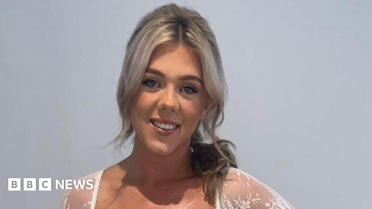 Amy Doherty who has light blonde hair partly pulled back over her left shoulder, she is wearing a white lace top and smiling at the camera.