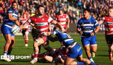 Gloucester's Will Trenholm is tackled during the Prem Rugby Cup match between Bath Rugby and Gloucester Rugby as players from both sides watch on