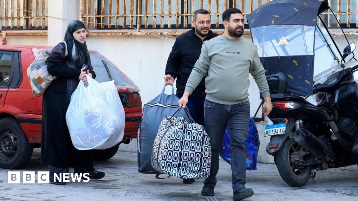 A woman and two men walk along a street in Beirut carrying big bags of belongings (03/03/26)