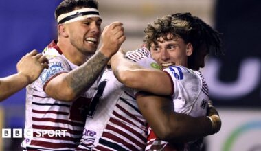 Noah Hodkinson (right, in Wigan's red-and-white kit) is hugged by Junior Nsemba after scoring a try, with two another team-mates joining the celebration