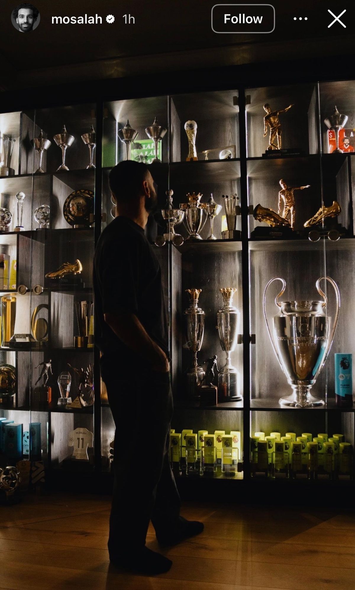 Mo Salah standing next to his trophy cabinet