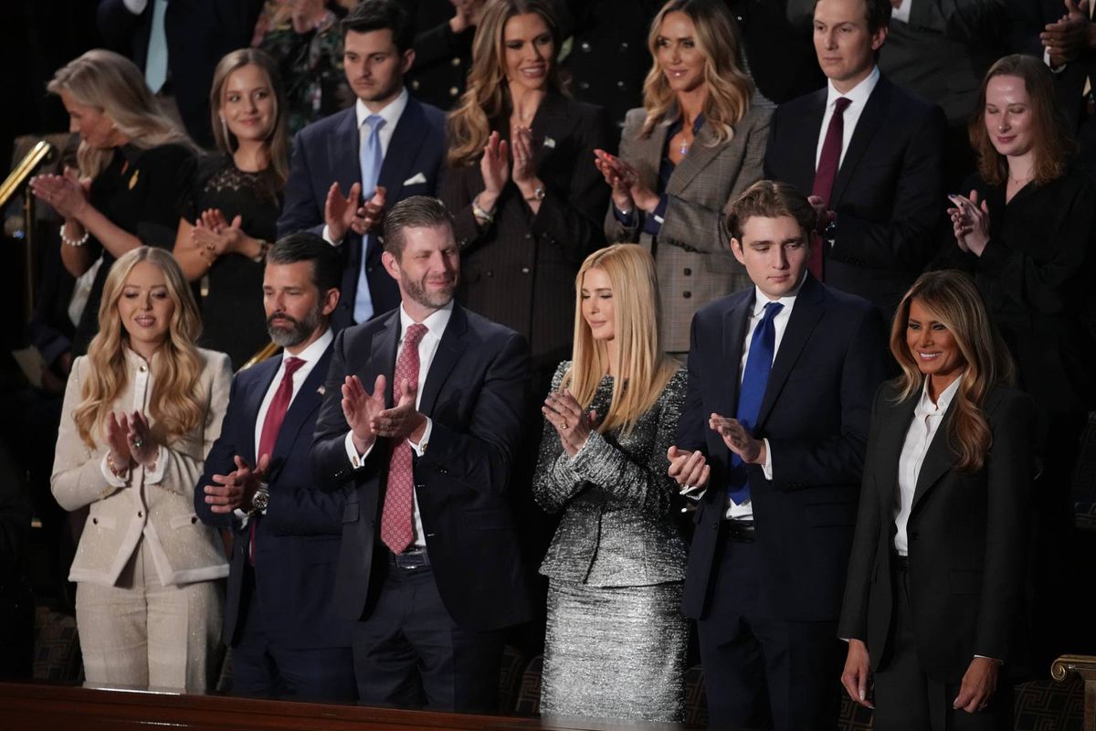 A group of formally dressed individuals, possibly politicians and their family members, are standing together in a room, clapping their hands.