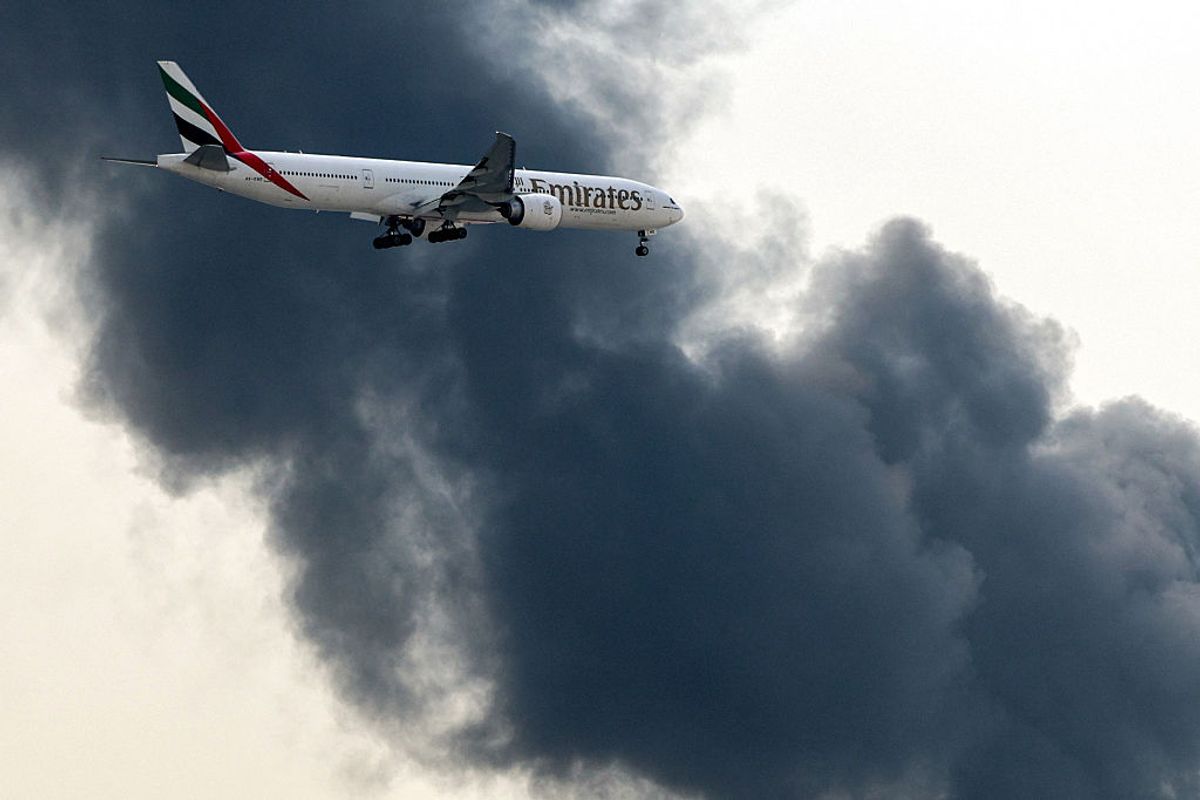 An Emirates Boeing 777 aircraft prepares for landing as a smoke plume rises from an ongoing fire at Dubai International Airport in Dubai on March 16, 2026. 