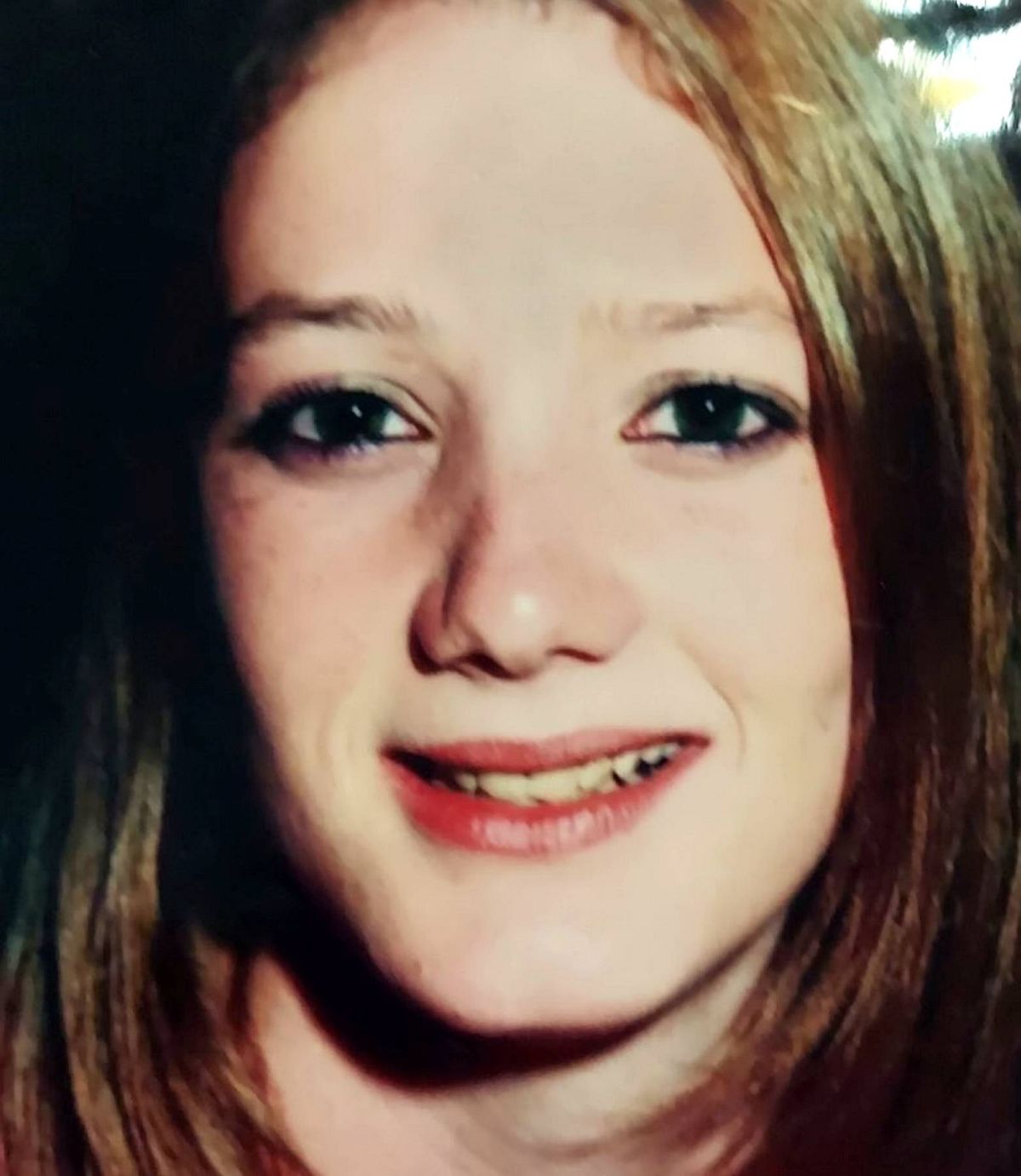 An individual with long, flowing hair and a radiant smile, their eyes sparkling with warmth and joy, captured in a close-up portrait that highlights their gentle expression and delicate features.