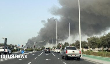 Several vehicles are seen on a multi-lane road in Abu Dhabi as smoke billows from Zayed port in the distance in the left of the picture