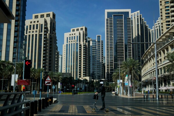 A man rides a battery powered scooter on a deserted road in Downtown Dubai, United Arab Emirates, Sunday, March 1, 2026. (AP Photo/Altaf Qadri)