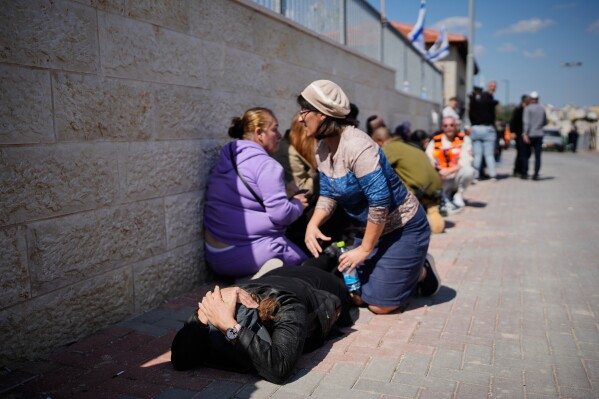 Mourners take cover while air-raid sirens warn of incoming missiles launched by Iran toward Israel during the funeral of Sarah Elimelech and her daughter Ronit who were killed in an Iranian missile attack, in Beit Shemesh, Israel, Monday, March 2, 2026. (AP Photo/Ohad Zwigenberg)