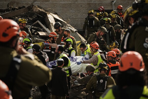 Rescue workers and military personnel carry a body of a victim from the scene where several people were killed by an Iranian missile strike in Beit Shemesh, Israel Sunday, March 1, 2026. (AP Photo/Leo Correa)