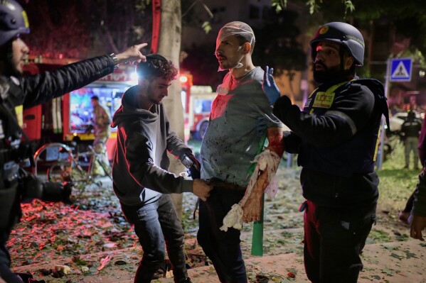 Rescue workers bandage a wounded man and provide first aid at the site of a direct hit from an Iranian missile strike in Tel Aviv, Israel, Saturday, Feb. 28, 2026. (AP Photo/Tomer Neuberg)