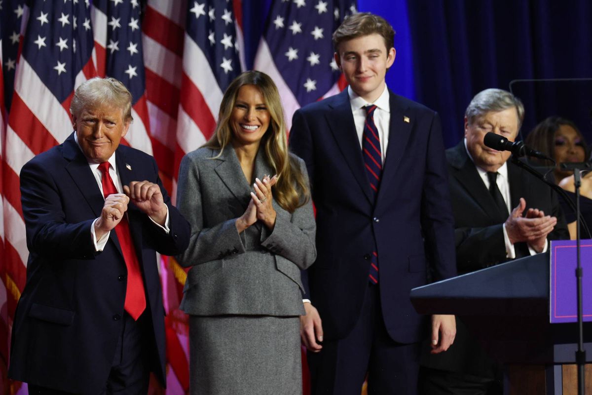 Several individuals, dressed in formal attire, stand in front of American flags, possibly at a political event. They appear to be clapping in unison, suggesting a moment of celebration or acknowledgment. A podium with a microphone is positioned in the foreground.