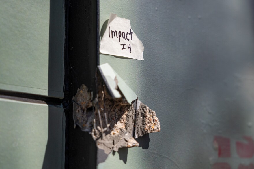 Part of a wall is damaged on the outside of a building. A police evidence tag sits above it.