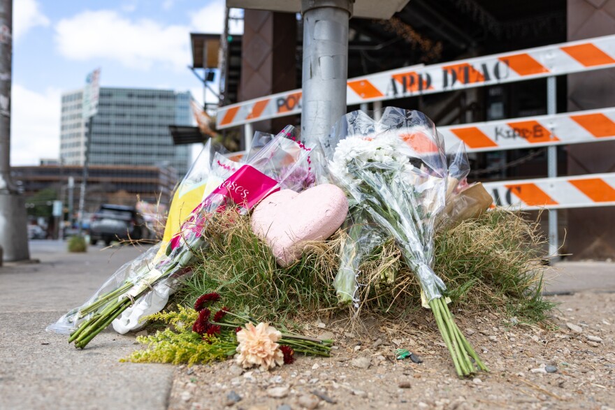 Flowers and pink heart sit outside a bar, leaning up against a pole.