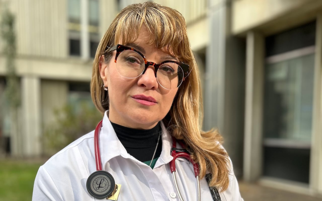 Female physician in white coat and stethoscope standing outside.