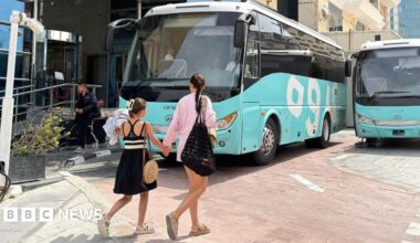 A woman and a girl walk in front of buses prepared for stranded airline passengers outside a hotel in Doha, Qatar. Photo: 1 March 2026
