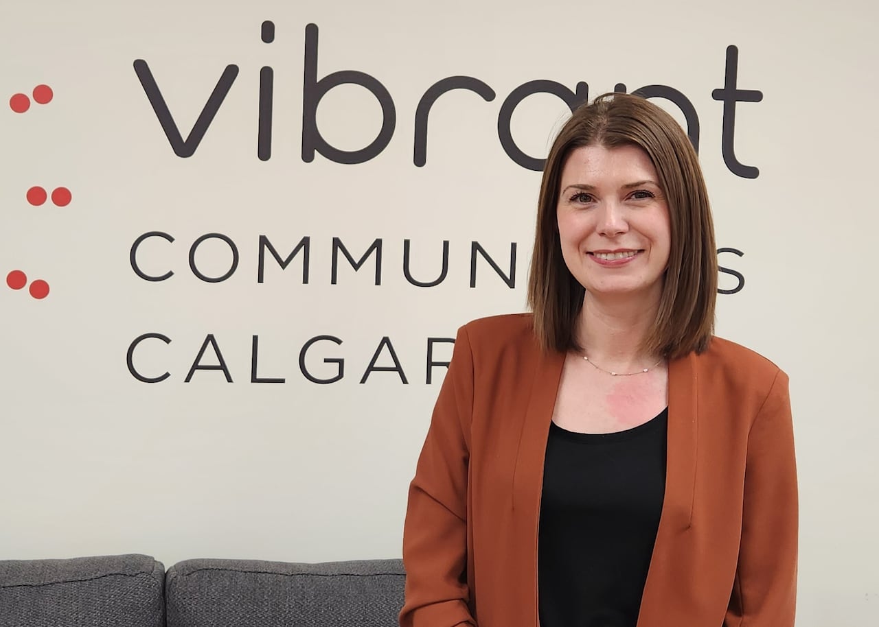 A woman stands in front of a sign that says Vibrant Communities Calgary. 