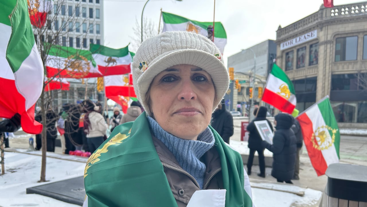 woman wrapped in wearing a green, white and red flag stands in the foreground while people wave the same flag behind her