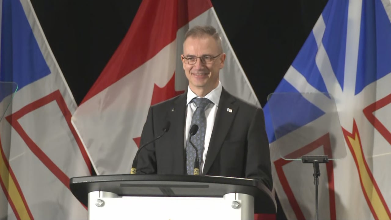 A smiling man wearing a suit stands at a podium. 