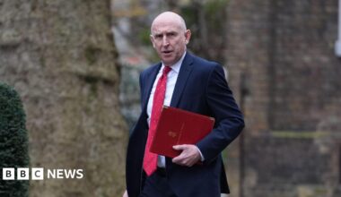John Healey looks towards the camera as he carries a red folder