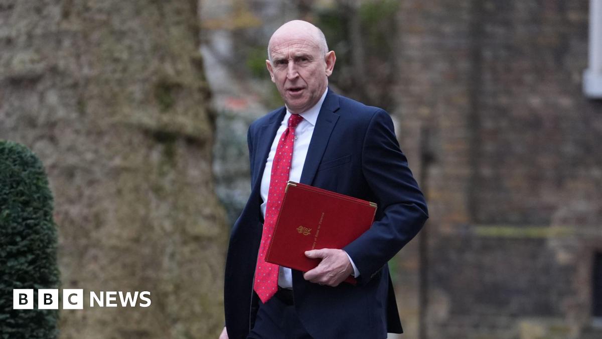John Healey looks towards the camera as he carries a red folder