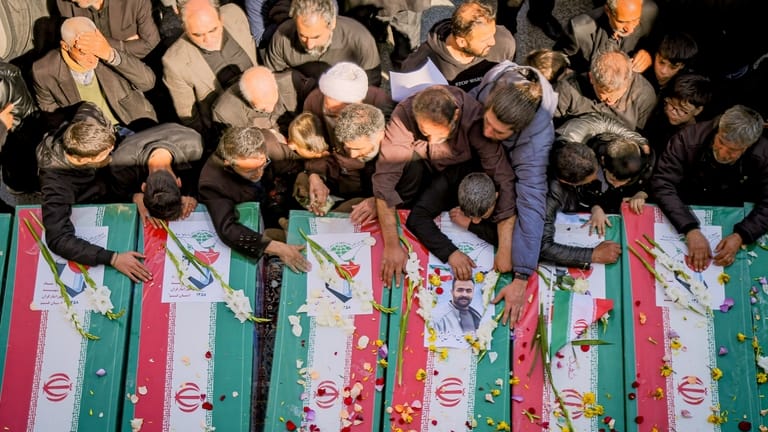 Mourners reach out to coffins during a funeral for people...