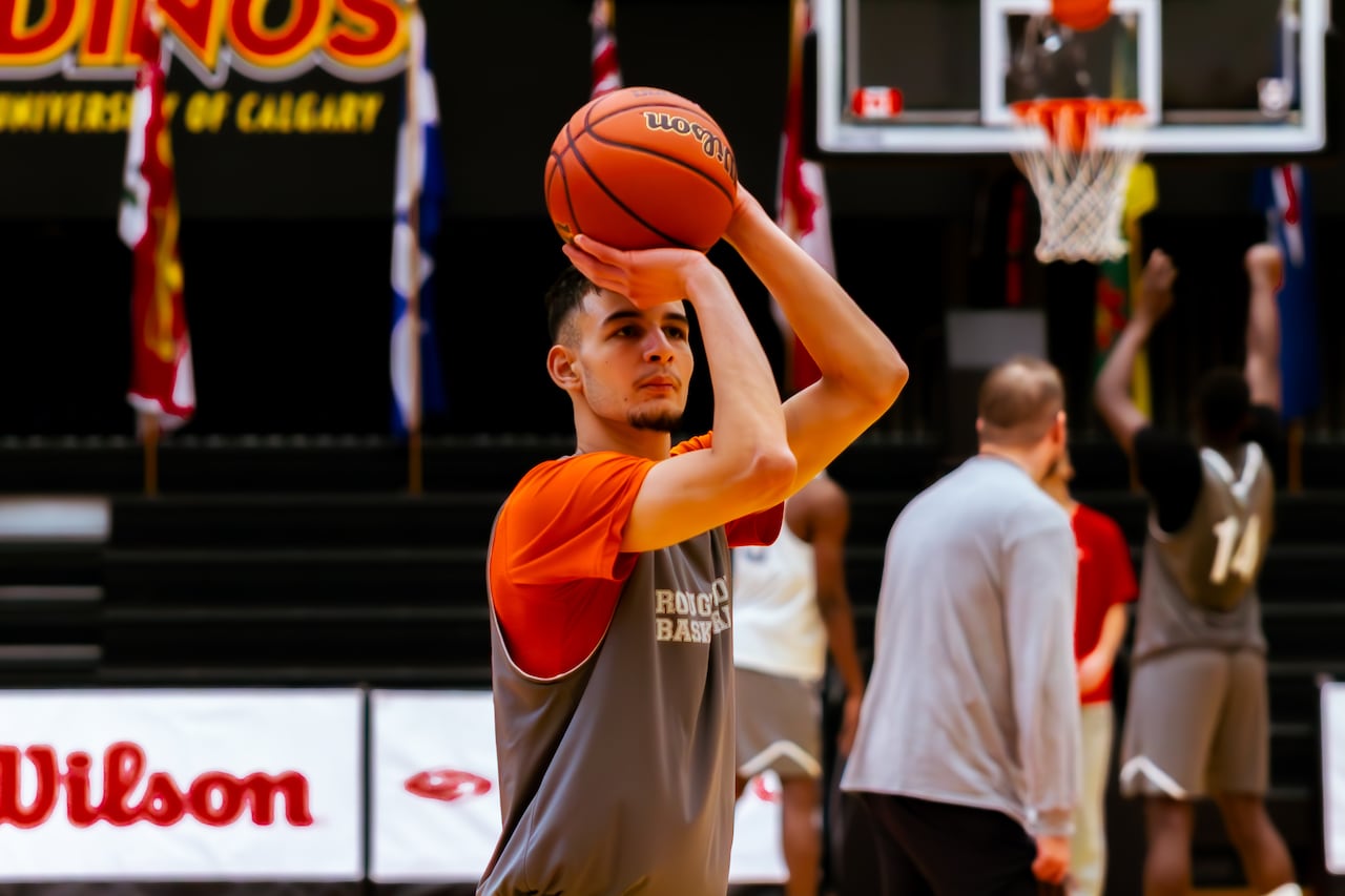 a college basketball player in grey and orange holds the ball just above his head as he prepares to shoot it