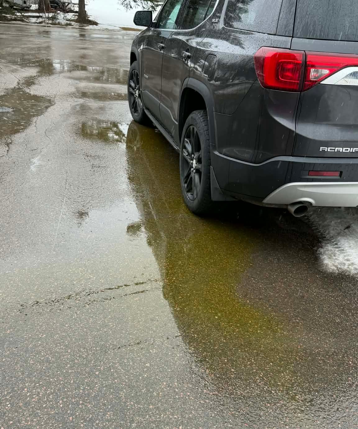A car parked in the street with yellow liquid coming from underneath.