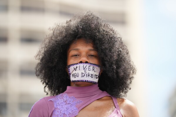 A woman with tape reading in Portuguese "Living is my right" over her mouth takes part in a march marking International Women's Day on Copacabana beach in Rio de Janeiro, Sunday, March 8, 2026. (AP Photo/Silvia Izquierdo)