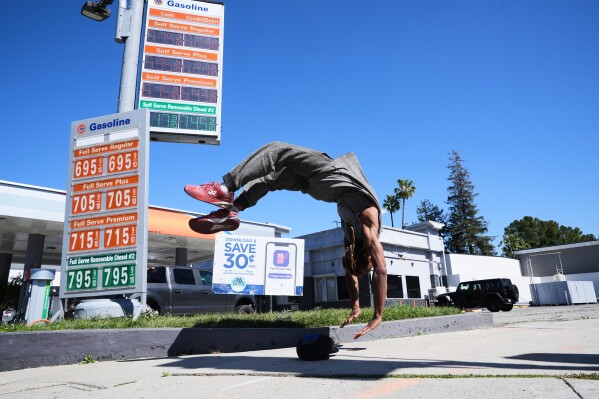 Marcus Hopkins, a street performer, does a backflip in front of advertised gas prices Monday, March 9, 2026, in Los Angeles. (AP Photo/Damian Dovarganes)