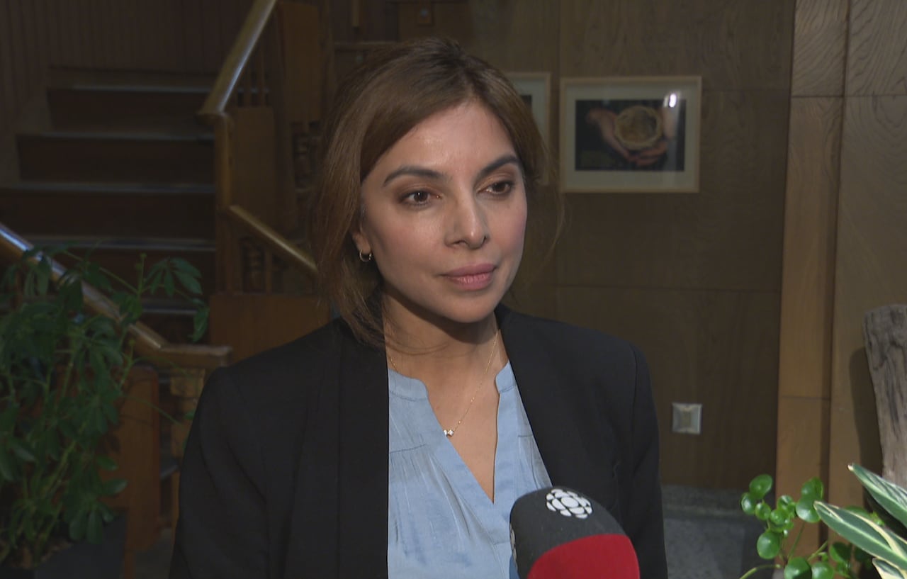 A woman with brown hair speaks in a wooden reception area.
