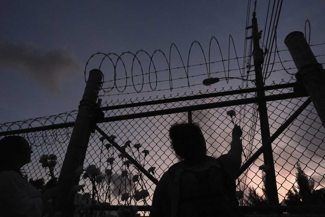 People place flowers on a fence outside Krome Detention Center in Miami in May 2025, during a vigil to recognize people who have died in U.S. Immigration and Customs Enforcement custody as well as those affected by mass deportations.