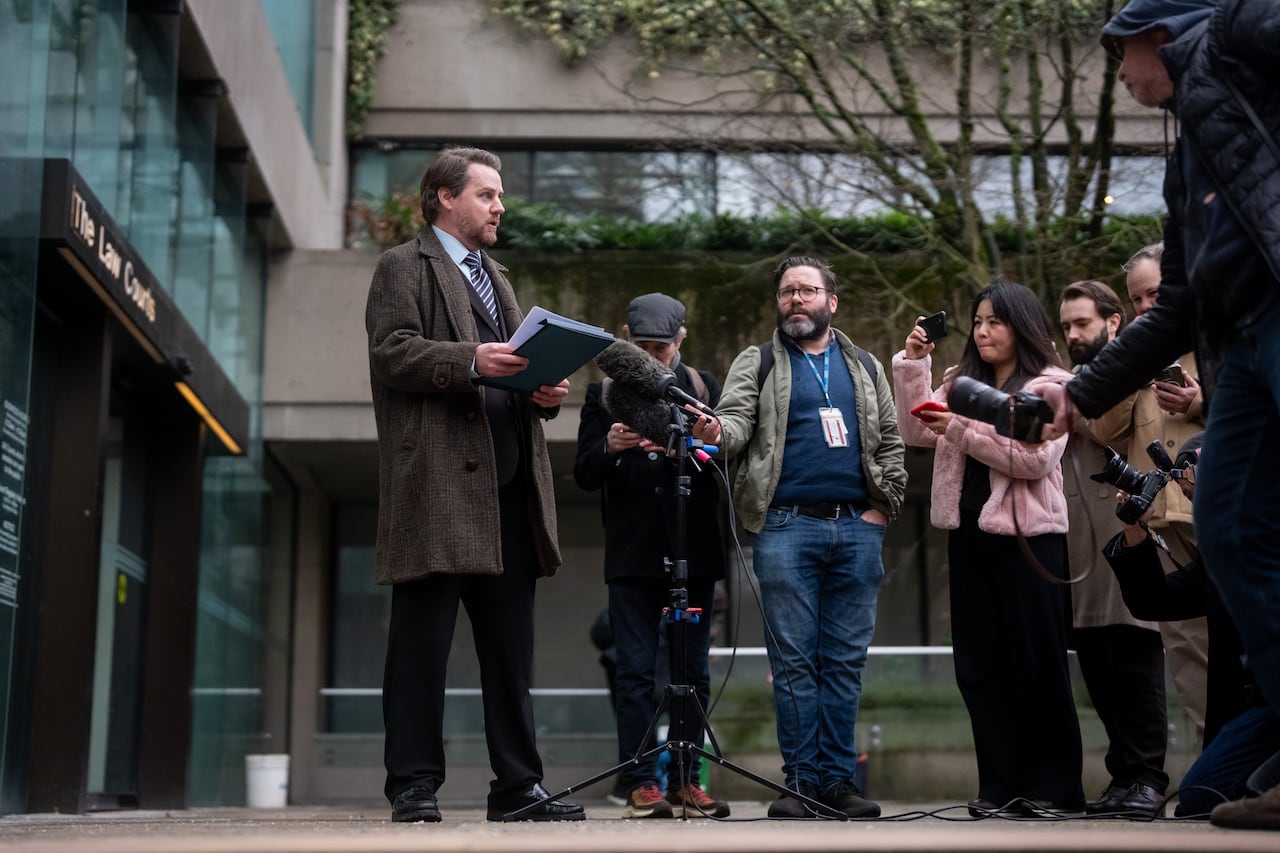 A man stands outside a courthouse speaking to media from a microphone.