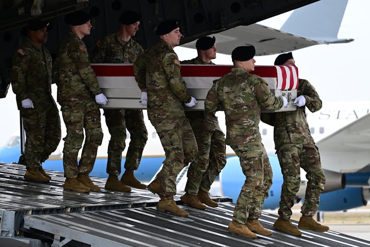 Several soldiers carry a coffin off a plane.