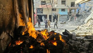A fire is seen in a structure on a heavily damaged city street.