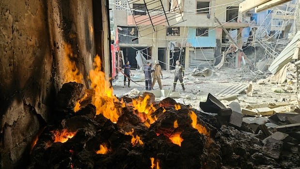 A fire is seen in a structure on a heavily damaged city street.