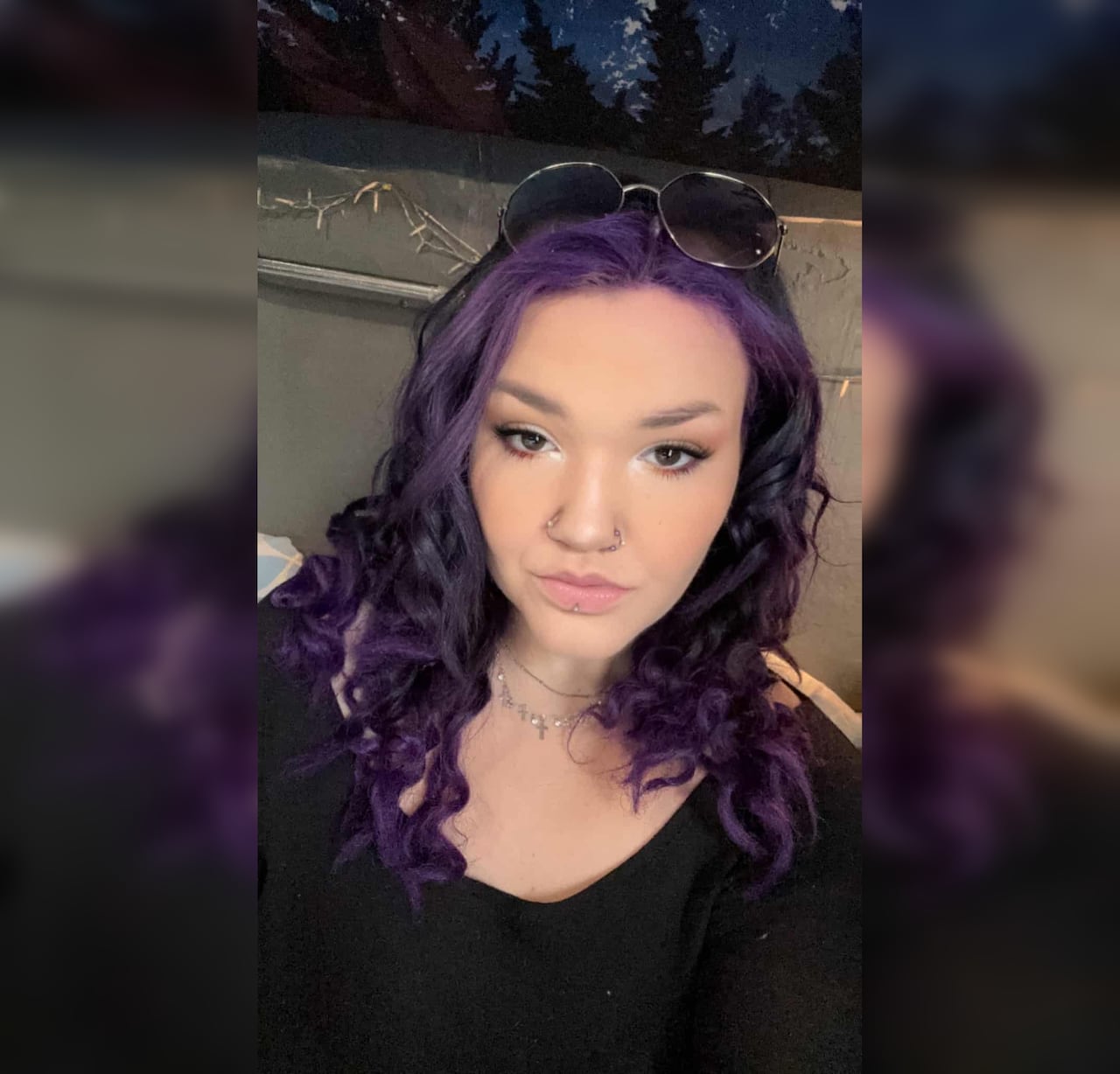 A woman with dark hair and purple streaks in her hair looks at the camera.