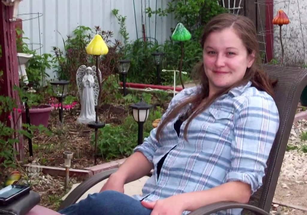 A woman sits in on a patio chair in a backyard.