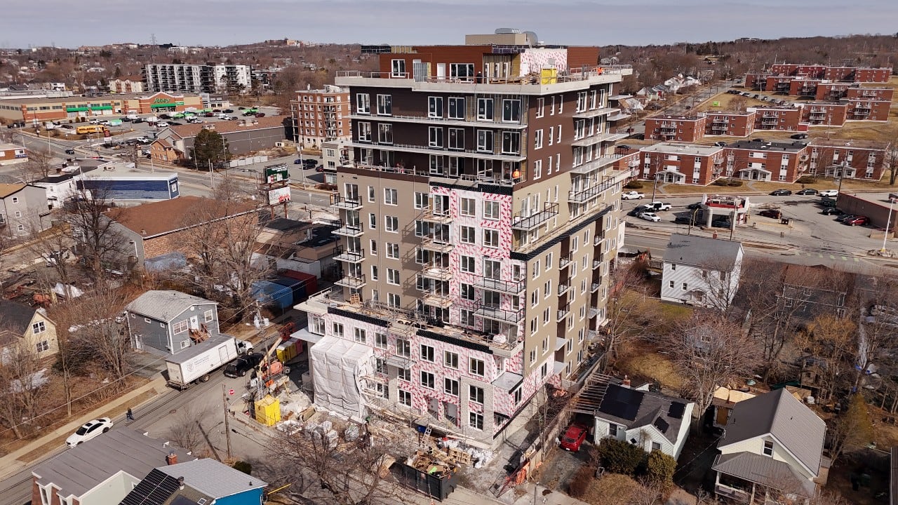 A tall apartment building under construction is seen from the air, with single-family homes surrounding it.