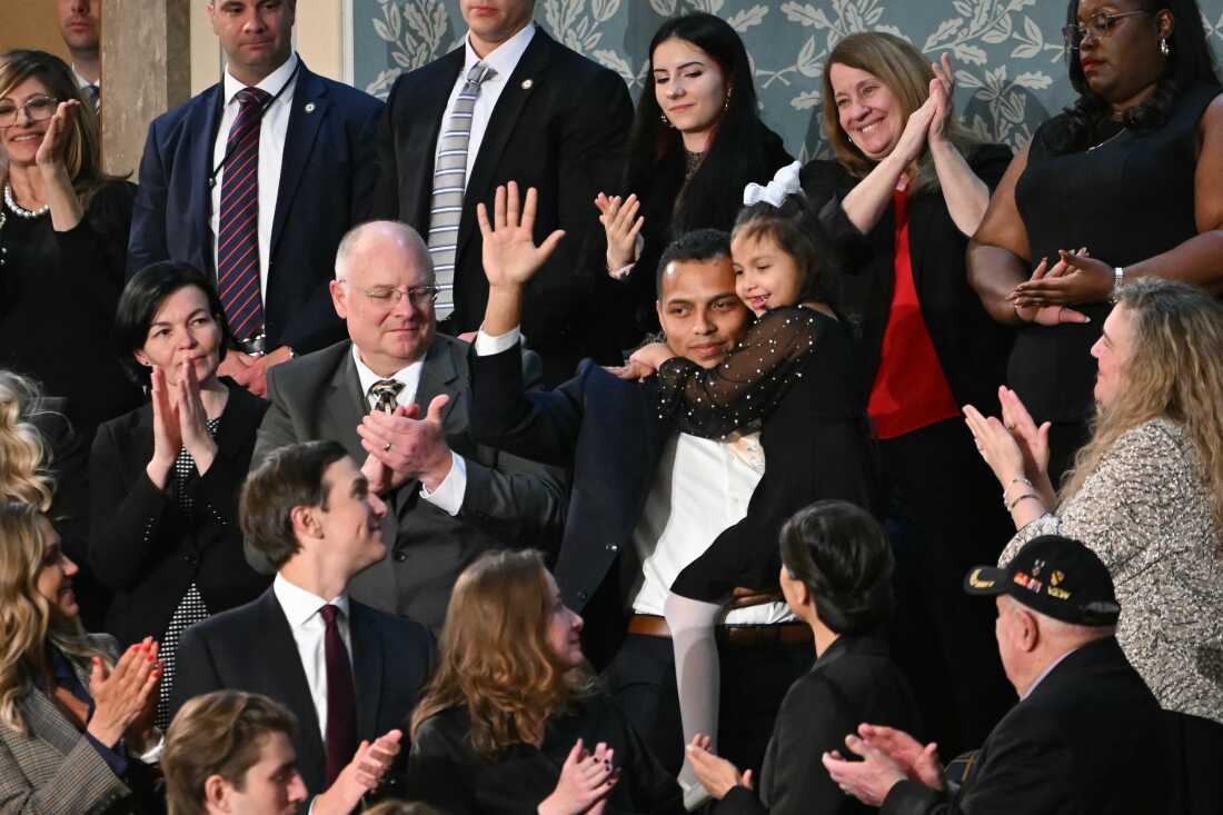 Seven-year-old Dalilah Coleman is held by her father, Marcus Coleman, as he holds up a hand in acknowledgment. Others in the audience turn to look at them.