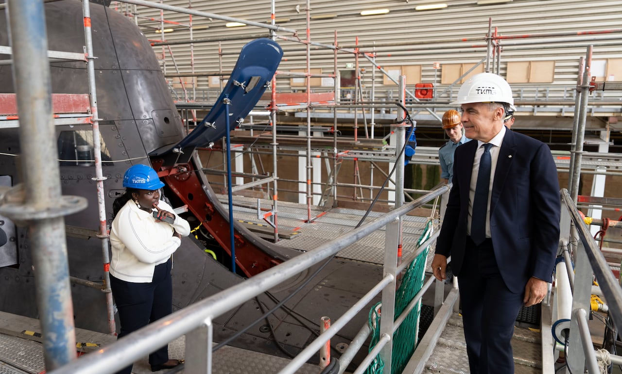 A man standing on a catwalk looks at the hull of a submarine