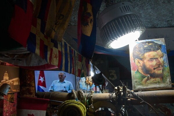 An image of Cuban Revolutionary hero Ernesto "Che" Guevara stands next to a TV showing Cuban President Miguel Diaz-Canel speaking, inside a souvenir shop in Havana, Cuba, Friday, March 13, 2026. (AP Photo/Ramon Espinosa)