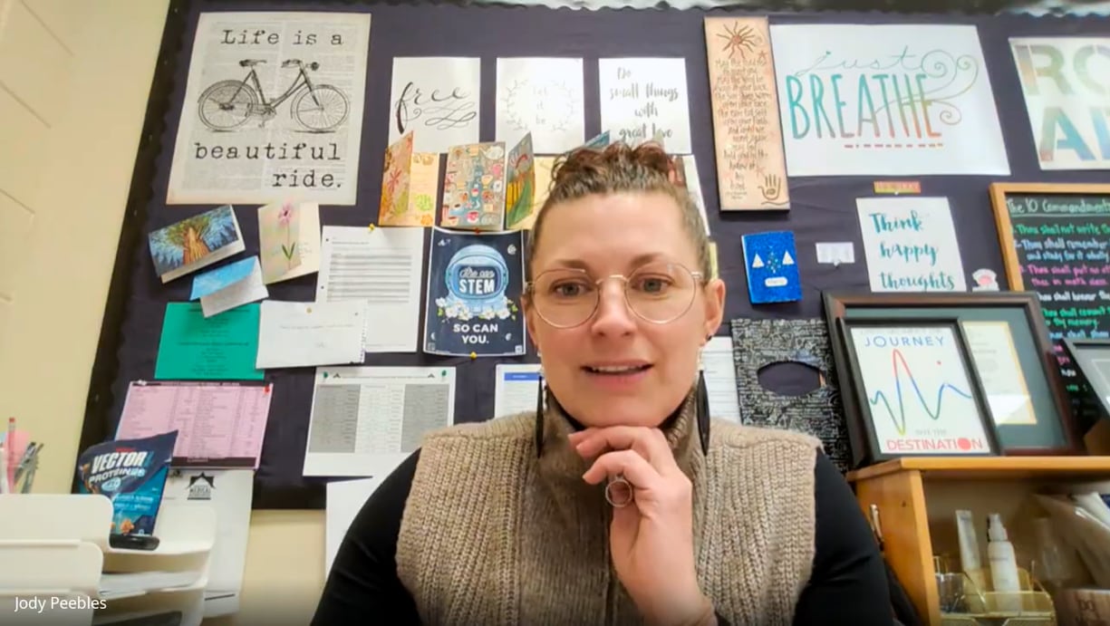 A woman sits in front of a bulletin board filled with art and inspirational sayings. 