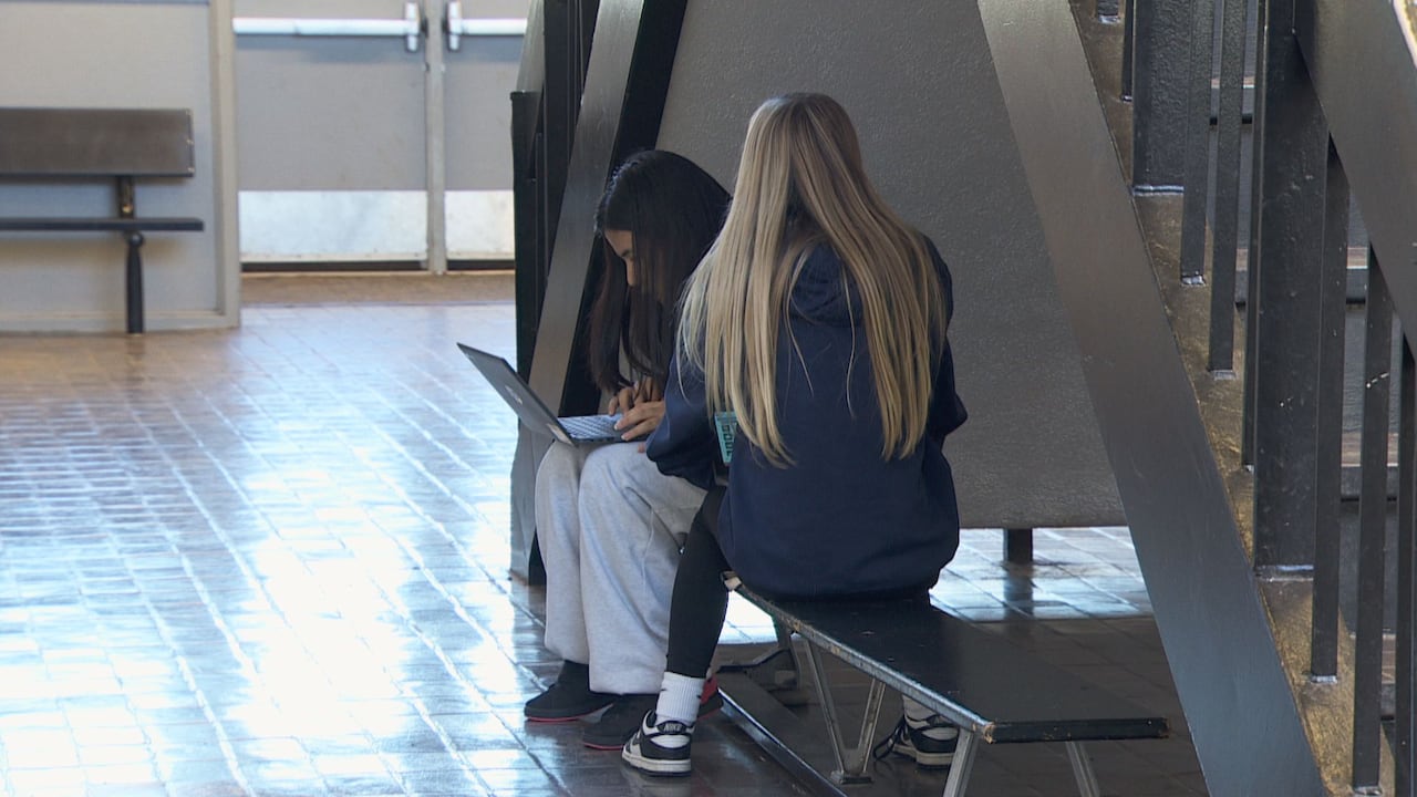 Two students sit on a bench in an empty hallway.