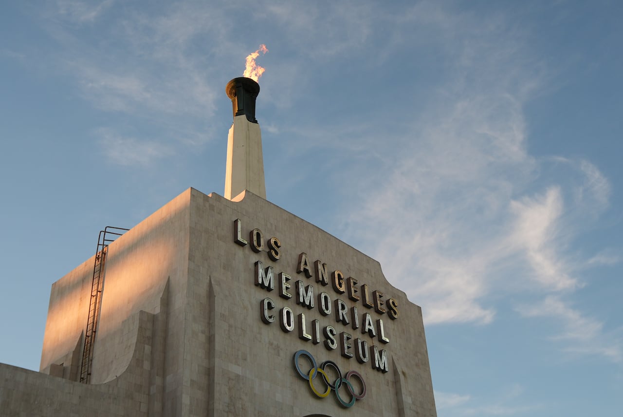 Flames are seen in a cauldron affixed to the top of a coliseum-like building.