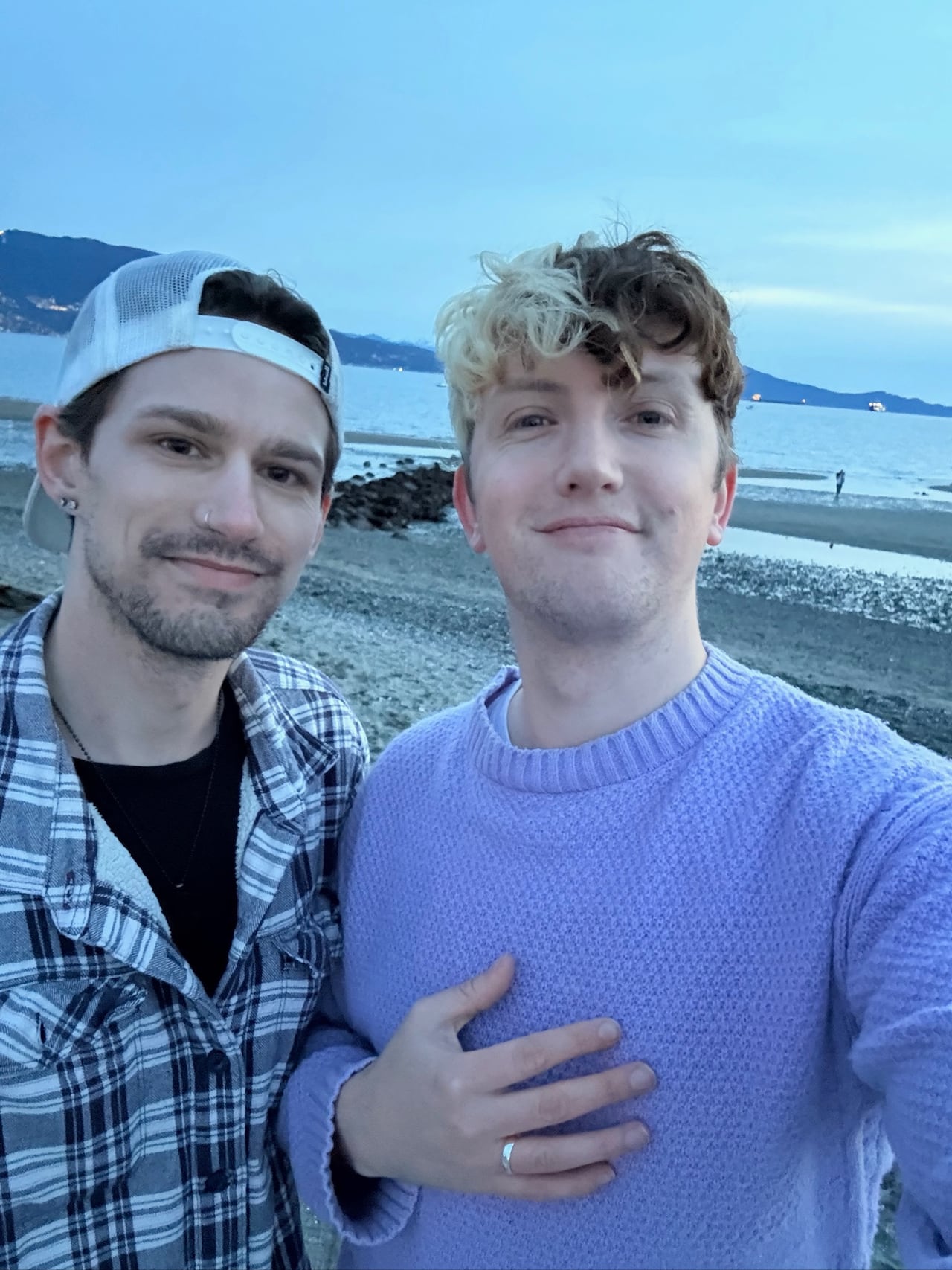Two smiling men pose for a photo on a beach