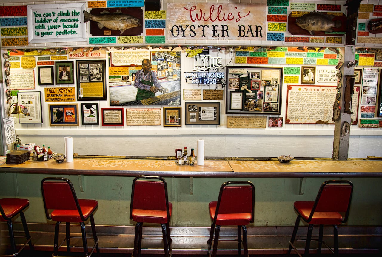A picture of dozens of signs on the wall above bar stools at an oyster house.