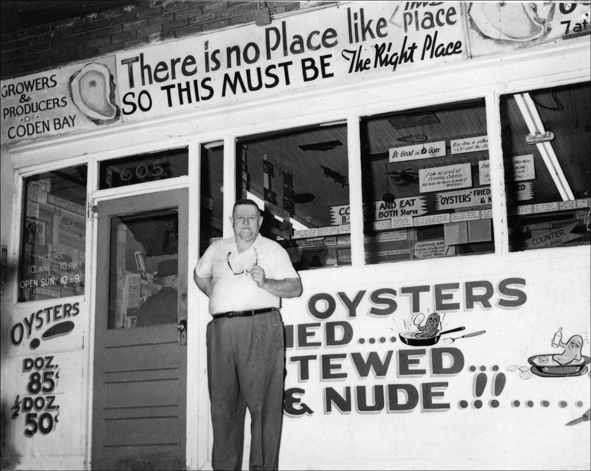 An archival black and white photo of J. Oliver Wintzell standing outside his restaurant, Wintzell's Oyster House