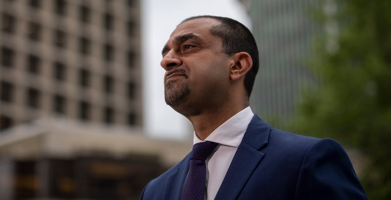 A South Asian man stares off to the left while being flanked by tall buildings in downtown Vancouver.