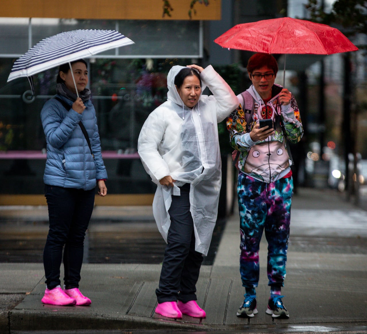 Three people, two of whom have umbrellas, are seen during a period of rain.
