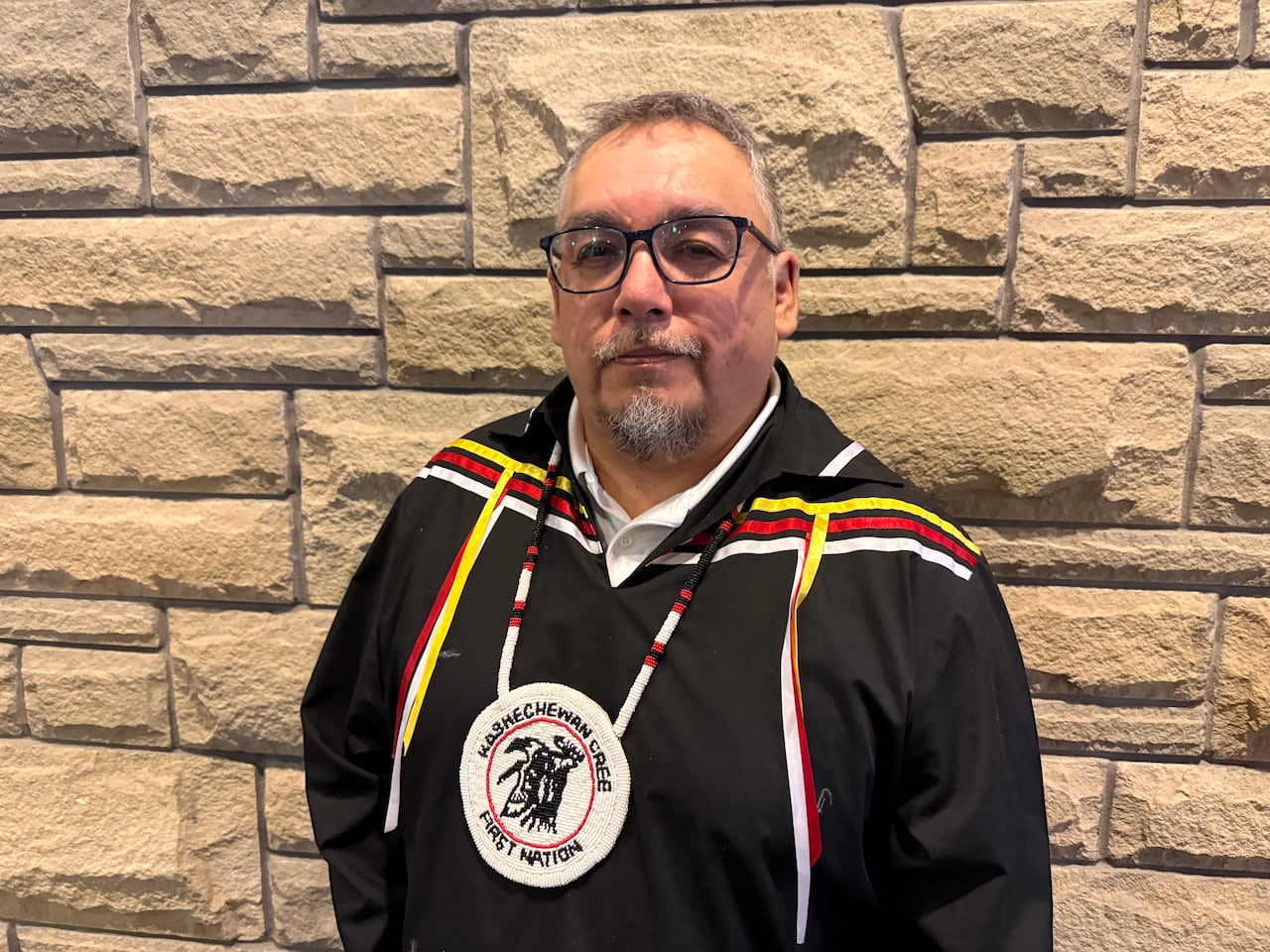 A man wearing a black shirt and a ceremonial necklace.