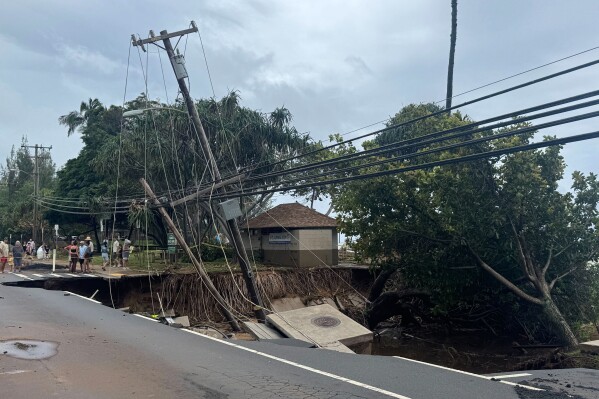 People gather near a collapsed road following severe storms on the island of Maui on Sunday, March 15, 2026, near the community of Weilea, Hawaii. (Athena Walsh via AP)